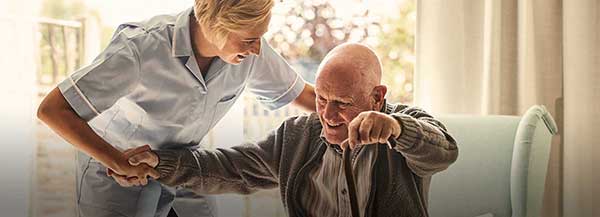 Sköterska hjälper en gammal man att ställa sig upp - Äldreomsorg