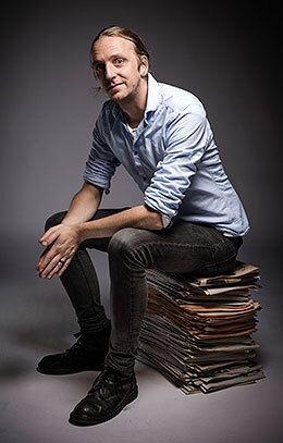 Porträtt av Martin Schibbye sittande på en hög med tidningar